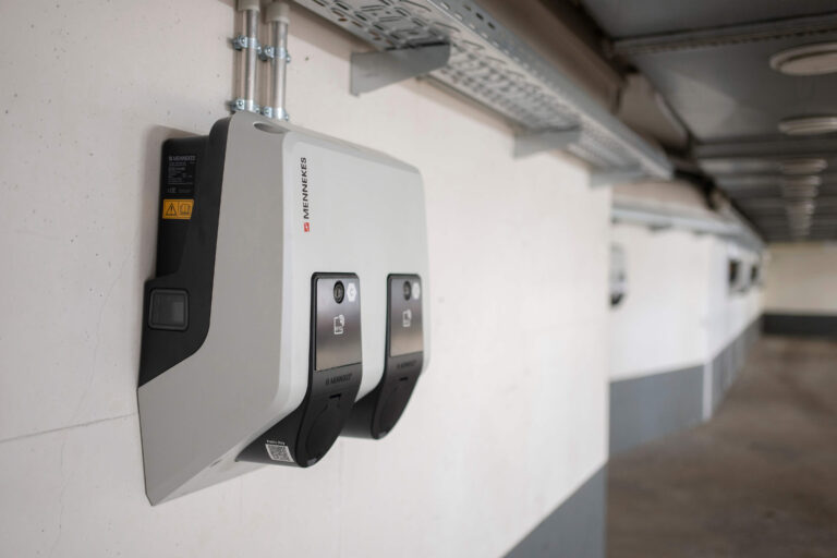 Seitliche Nahaufnahme einer Mennekes-Ladestation mit zwei Ladepunkten, montiert an der Wand eines überdachten Parkhauses.